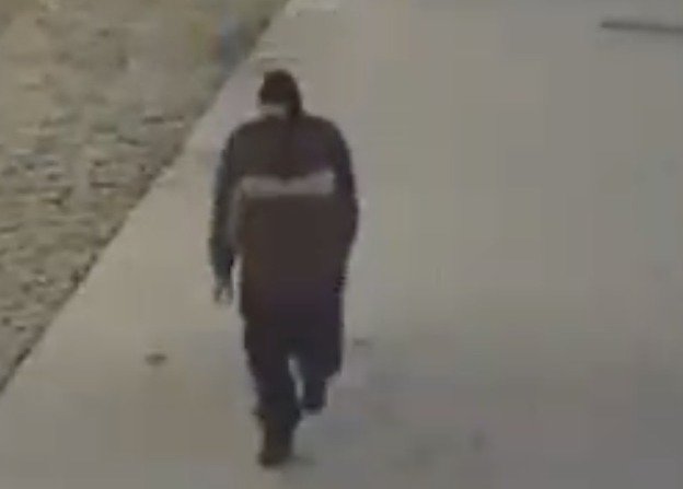 A man in a black mask and dark jacket and pants captured on surveillance footage