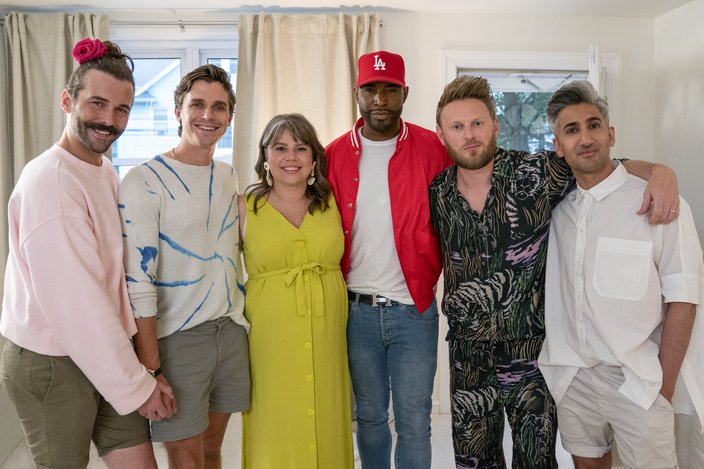 Five men and one woman in a bright green dress stand together in a white room
