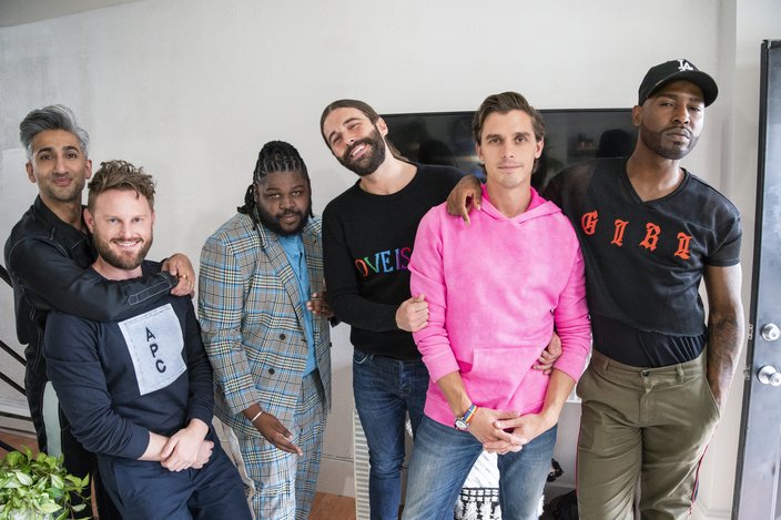 Six men stand inside a room with white walls