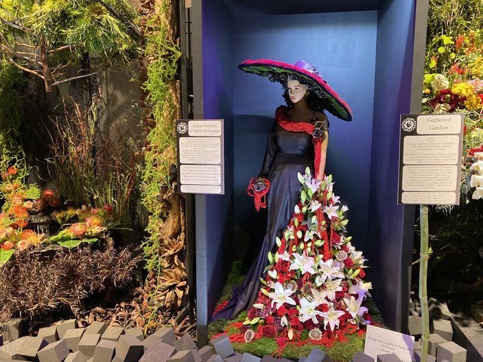 Mannequin wearing a black and red hat and dress with spray of white lilies