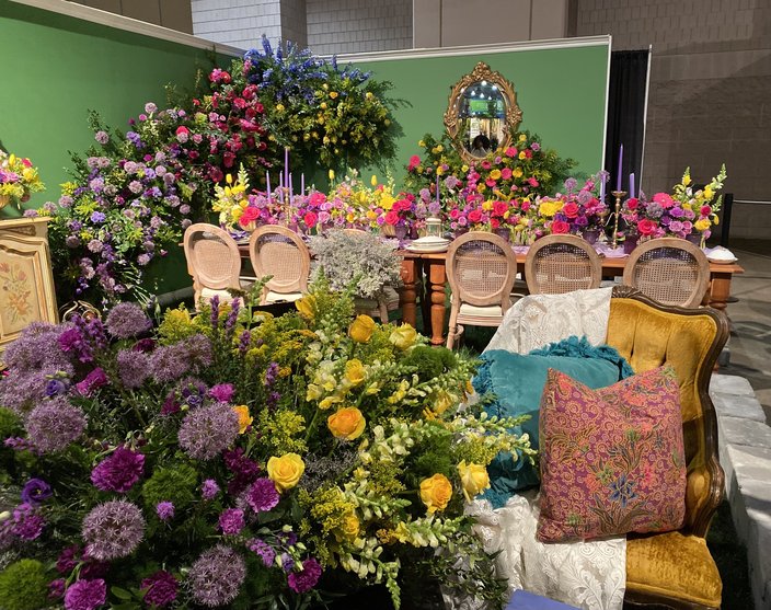 'Need for Ceremony' exhibit of yellow, purple, blue and pink flowers on a dining table and chairs