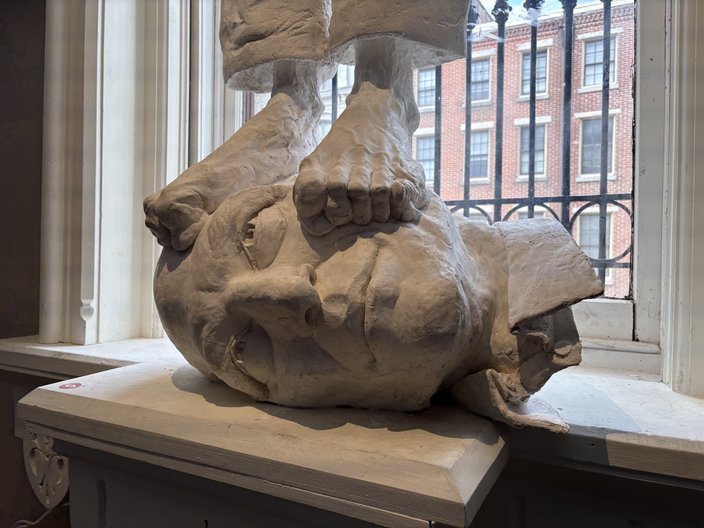 White sculpture of a man's head turned on its side with a pair of feet atop it