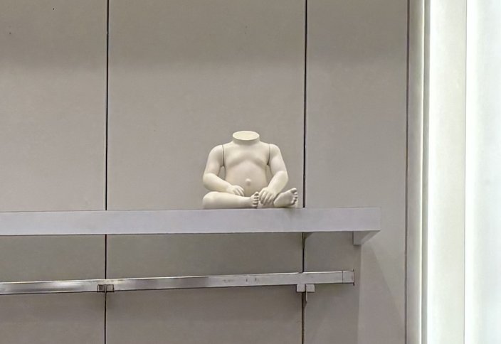 A white headless baby mannequin sits on a gray shelf