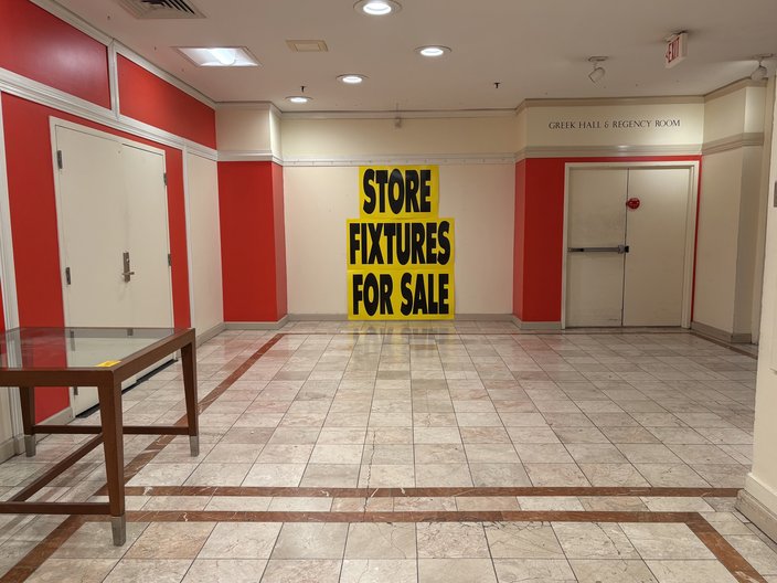 An empty department store hall with a yellow sign reading 'STORE FIXTURES FOR SALE'