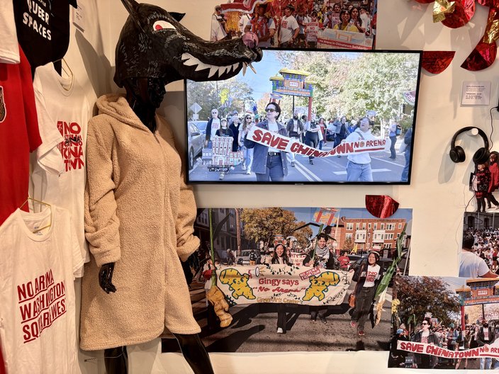 A video screen plays footage from No Arena in Chinatown protests in Philadelphia. It is surrounded by T-shirts, photos and a large wolf prop