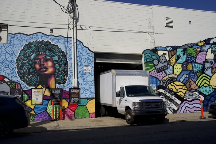 A white truck exits a white building with a painted mural