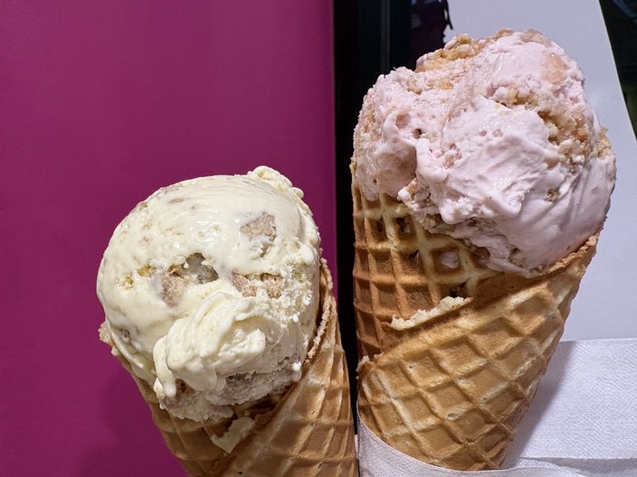 Two ice cream cones in front of a pink, white and black wall