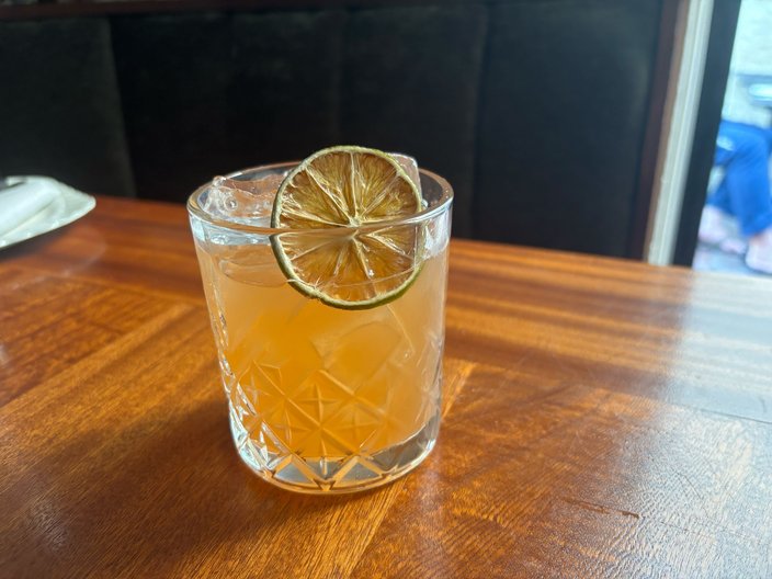 Peach-colored cocktail in a rocks glass with ice and a lime wheel on a brown table