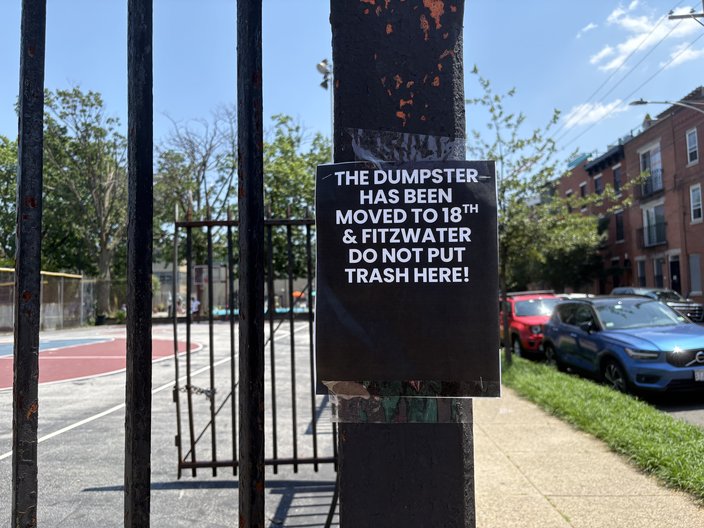 Dark sign with white text reading, 'THE DUMPSTER HAS BEEN MOVED TO 18TH & FITZWATER DO NOT PUT TRASH HERE!' taped to a pole