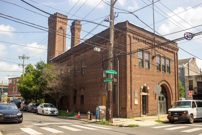 Large brick firehouse on a street corner with parked cars in front of it.