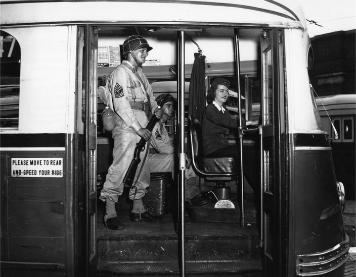 Black and white photo of two soldiers at the front of a trolley car, driven by a woman.