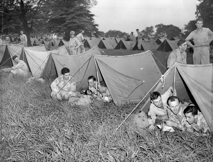 Black and white photo of soldiers lying in the grass under tents.