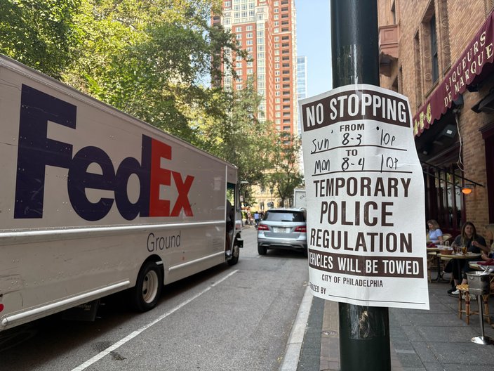 Black and white sign reading NO STOPPING taped to a pole. A FedEx truck is visible to the left.