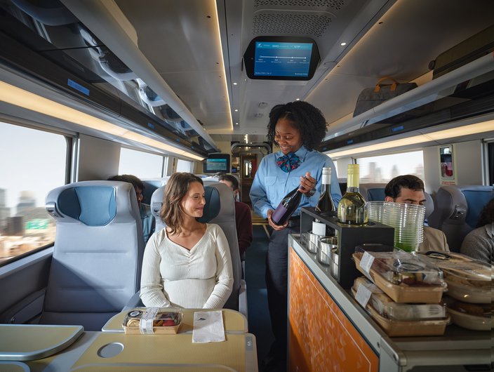A woman in a blue shirt offers a woman in a white shirt a bottle of wine from the cafe cart aboard the new Amtrak Acela train