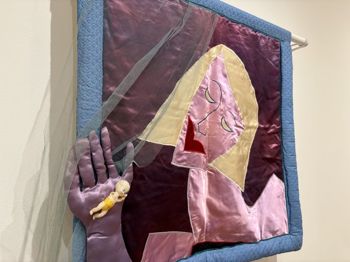 A textile portrait of a blonde woman with a purple gloved hand breaking out of the blue frame