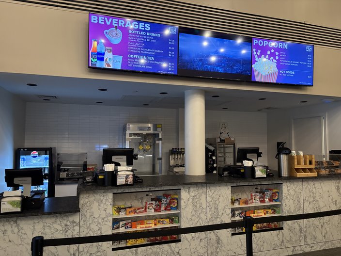 A movie theater concession counter with three screens displaying items