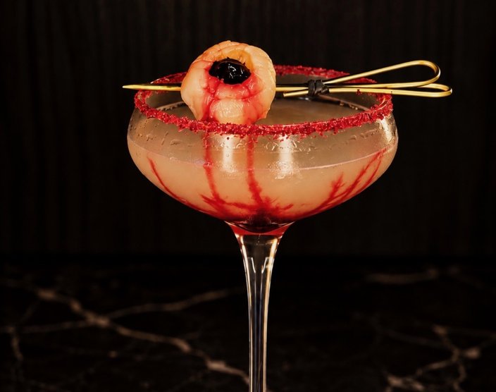 Halloween cocktail in a coupe glass with a red rim and garnish resembling an eyeball