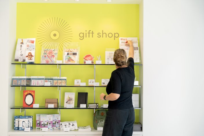 A woman in black stands in front of a white and green gift shop display wall