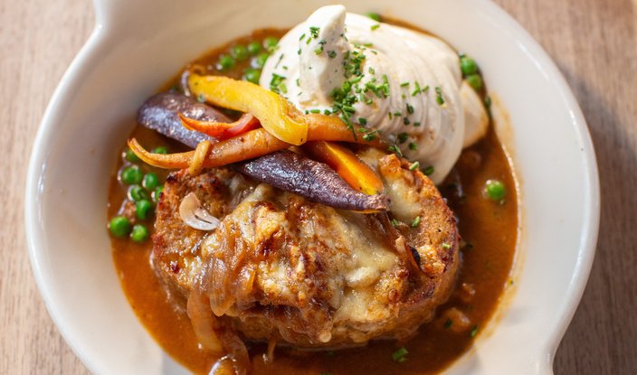 Meatloaf in a white dish with multi-colored carrots, green peas and mashed potatoes