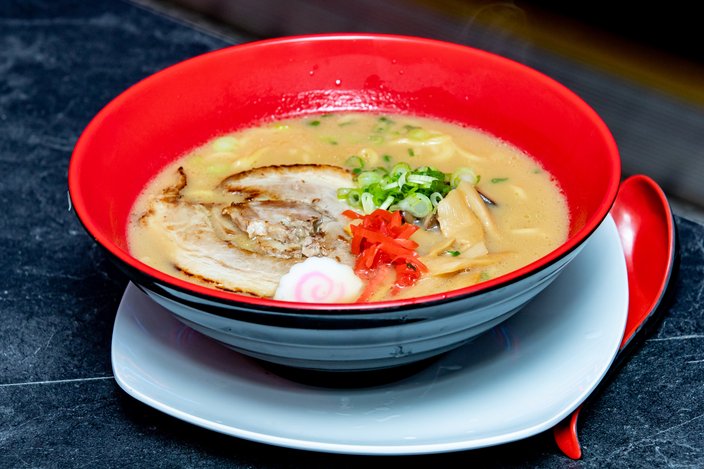 A red bowl of ramen soup on a white dish