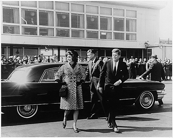 Black-and-white photo of Jacqueline Kennedy in a leopard skin coat and President John Kennedy in a suit.