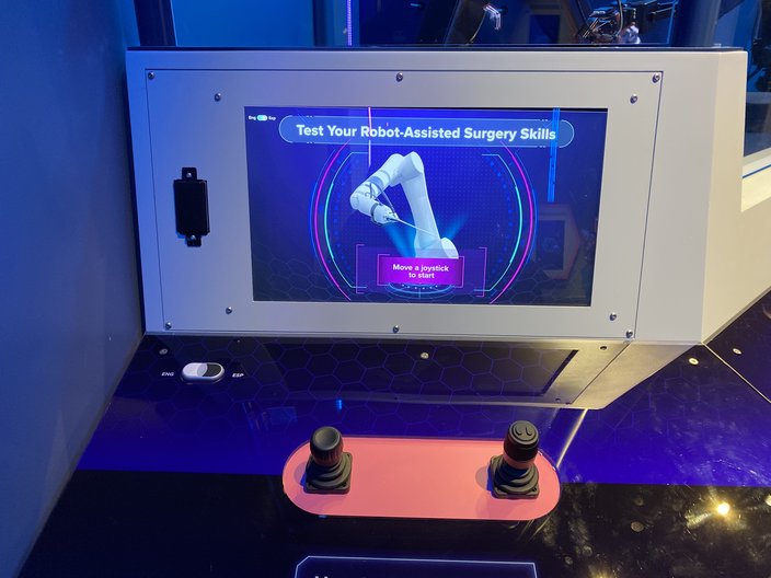 Computer screen with text reading 'Test Your Robot-Assisted Surgery Skills' and two black joysticks.