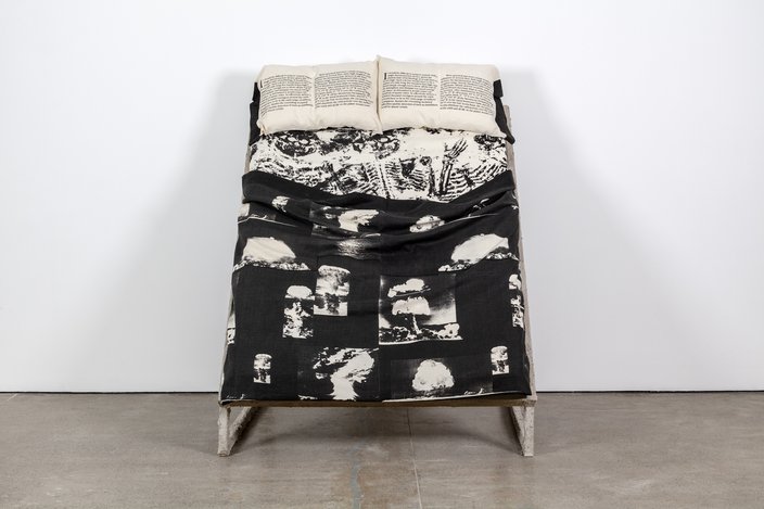 A bed with two pillows covered in black-and-white sheets printed with nuclear bombs and skeletons.