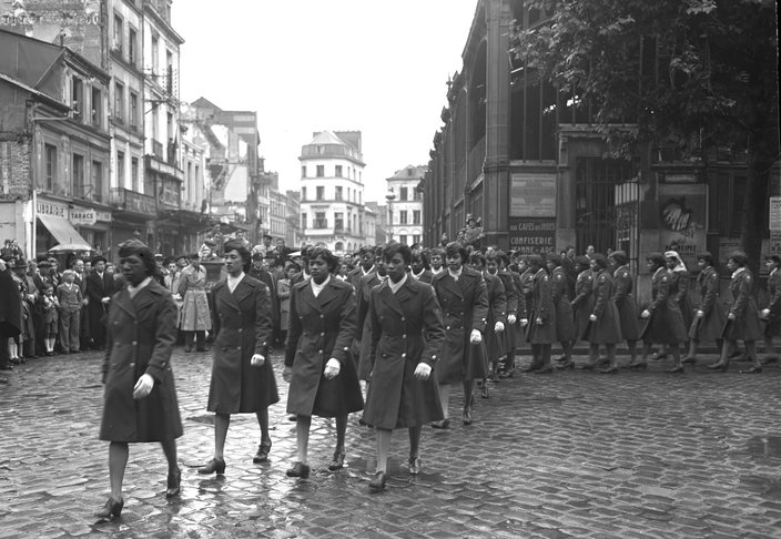 A black-and-white photo of Black women in military uniforms walking in formation through a cobblestone street