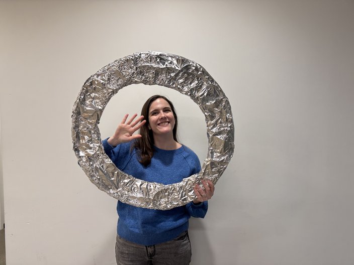 Woman in a blue sweater waves and holds an aluminum foil hoop