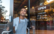 Happy waiter opening on the doors at a cafe