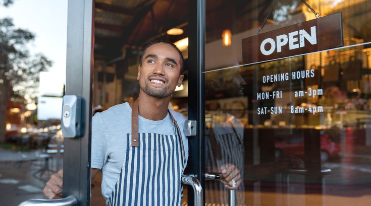 Happy waiter opening on the doors at a cafe
