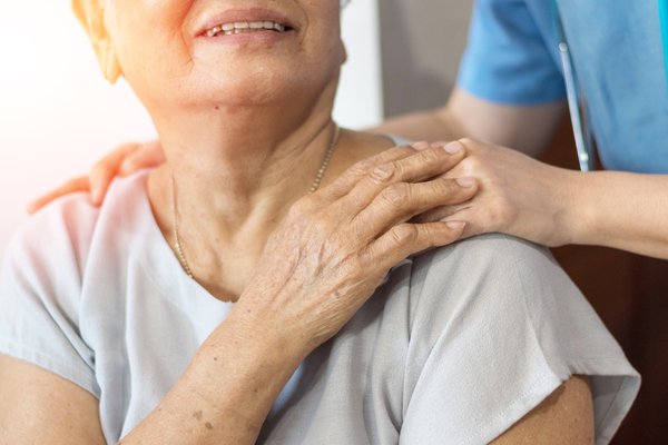 Elderly female hand holding hand of young caregiver at nursing home.