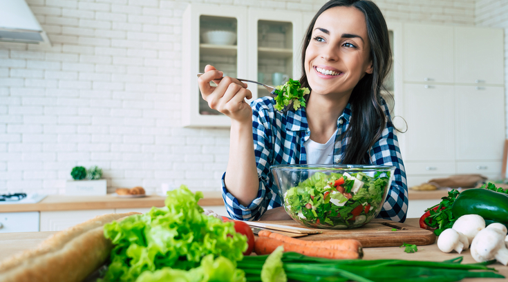 Purchased - a woman eating a salad smiling in her kitchen