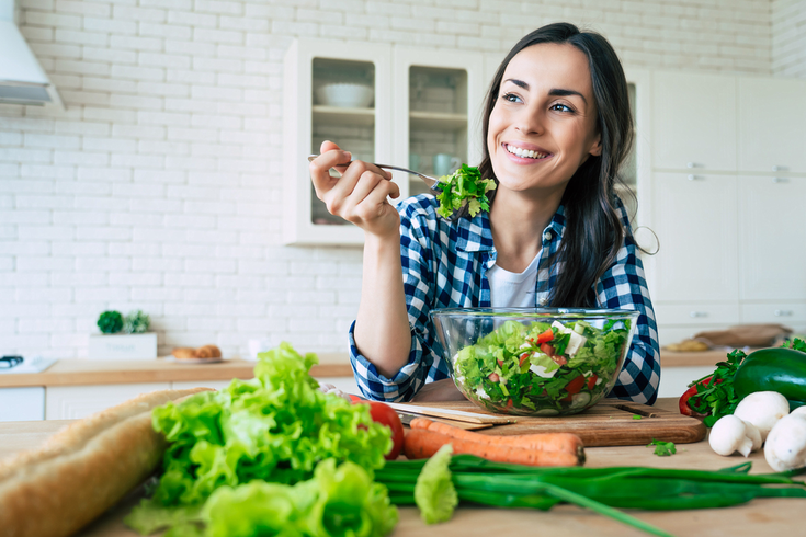 Purchased - a woman eating a salad smiling in her kitchen