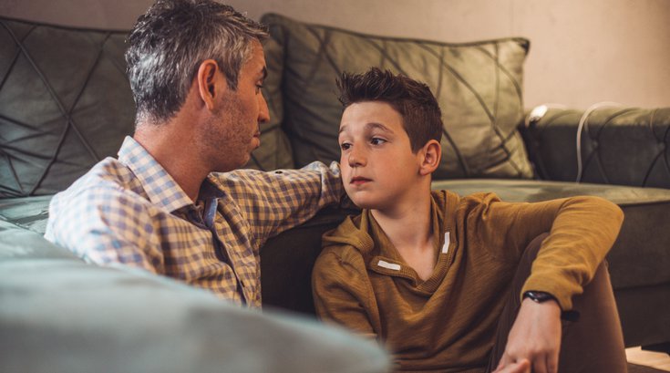 Father talking with teen son in living room
