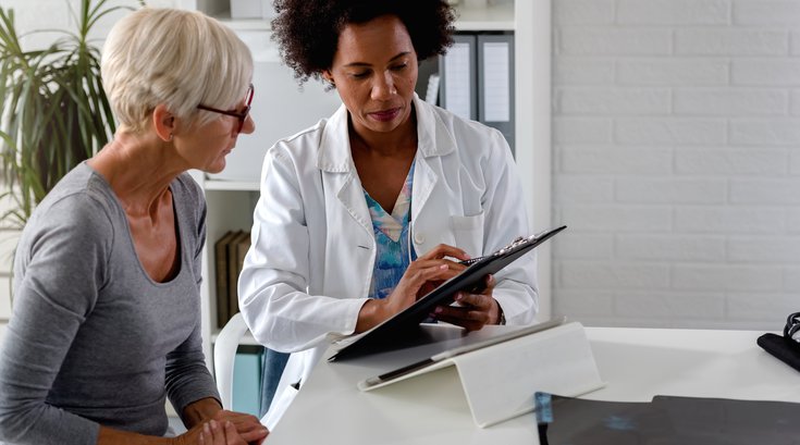 Purchased - A female doctor sits at her desk and chats to an elderly female patient