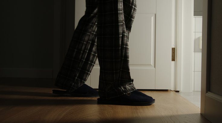 Aged man in a pajamas and slippers walks to a bathroom at home