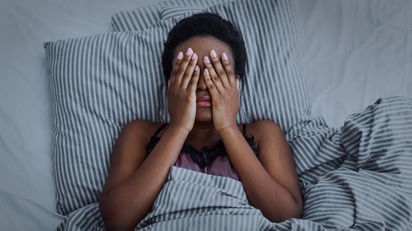 Laying in bed with hands over face worrying