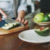 Purchased - Female hands cut avocado on wooden working surface in kitchen at the home stock photo