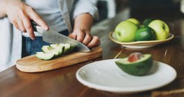 Purchased - Female hands cut avocado on wooden working surface in kitchen at the home stock photo