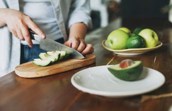 Purchased - Female hands cut avocado on wooden working surface in kitchen at the home stock photo