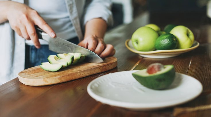 Purchased - Female hands cut avocado on wooden working surface in kitchen at the home stock photo