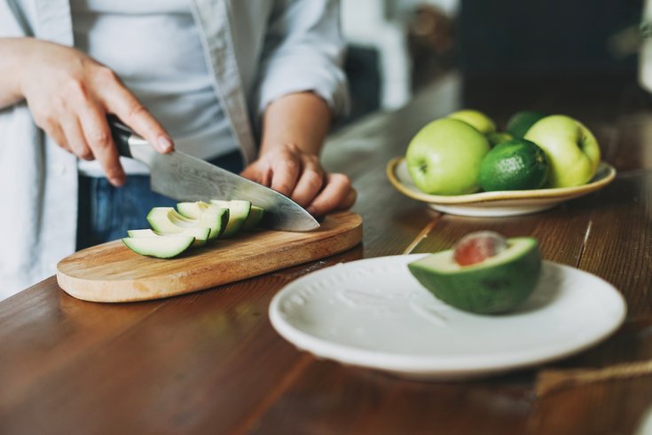 Purchased - Female hands cut avocado on wooden working surface in kitchen at the home stock photo