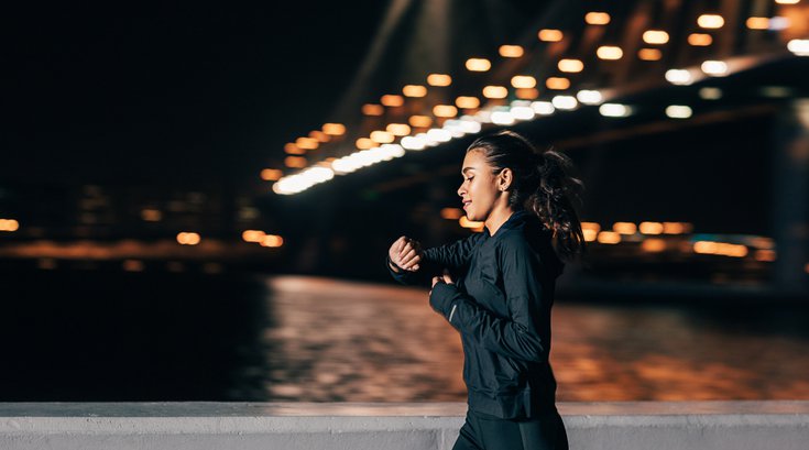 Purchased - woman jogging at night looking at fitness tracker