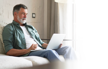 Purchased - Older man sitting on a sofa on laptop