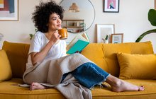 Purchased - woman reading a book at home, drinking coffee sitting on the couch