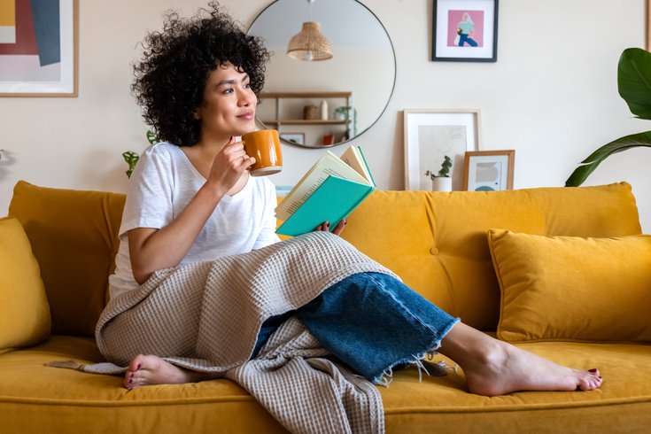 Purchased - woman reading a book at home, drinking coffee sitting on the couch