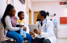 Purchased - doctor using touchpad while talking to mother and her son in waiting room