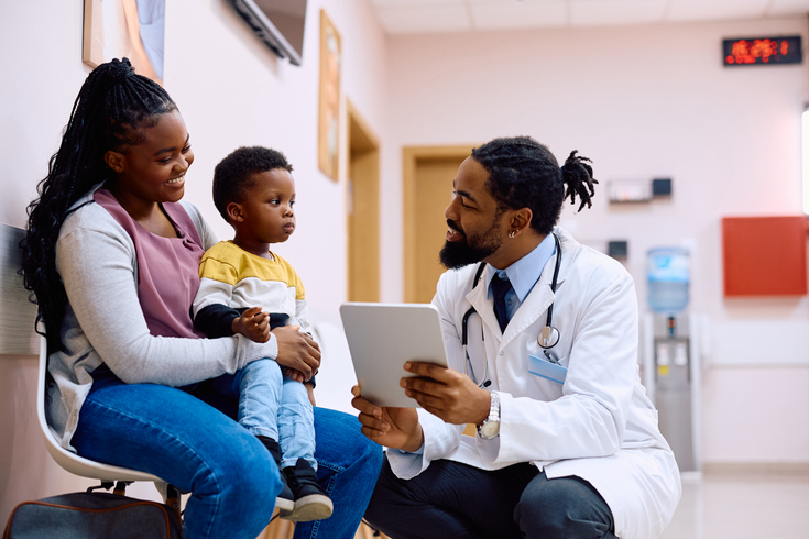 Purchased - doctor using touchpad while talking to mother and her son in waiting room