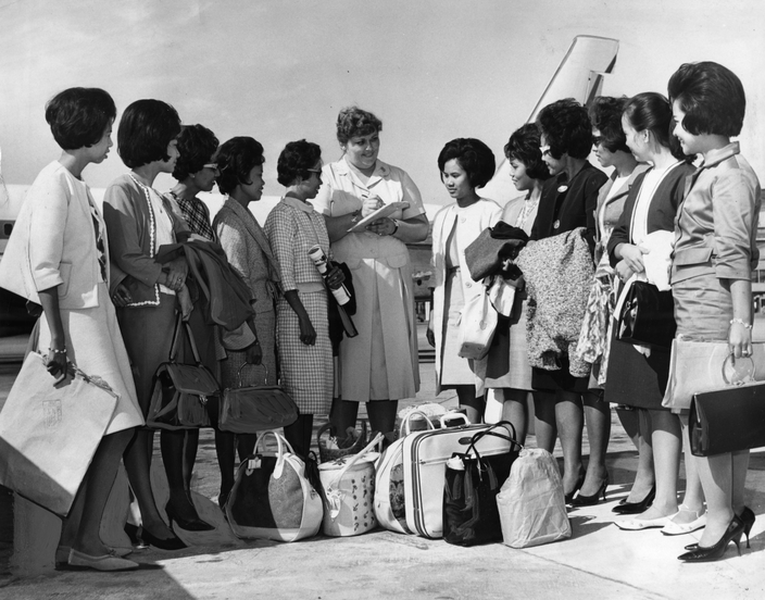 12 women stand on the airport tarmac with their bags in the center